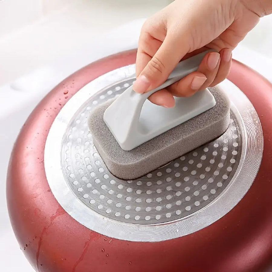 Hand using a palm-grip scrub brush on the bottom of a pan